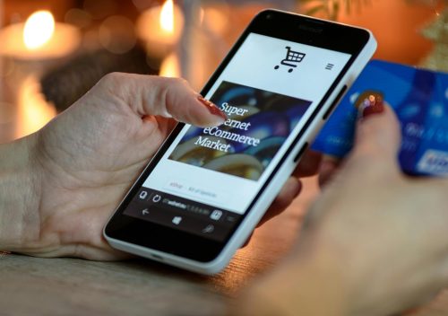 Woman using smartphone for online shopping with credit card in hand, festive background lighting.