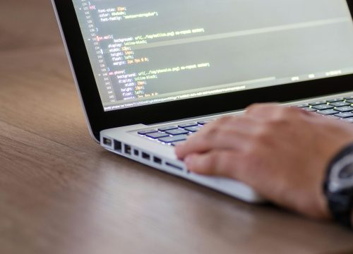 Person coding on a laptop with HTML code on screen, showcasing development work.